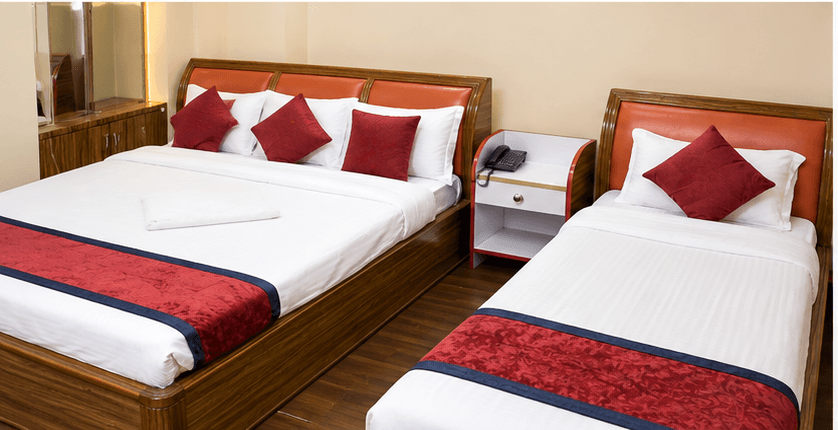 Hotel Taj guest room with a double bed and a single bed dressed in white and burgundy